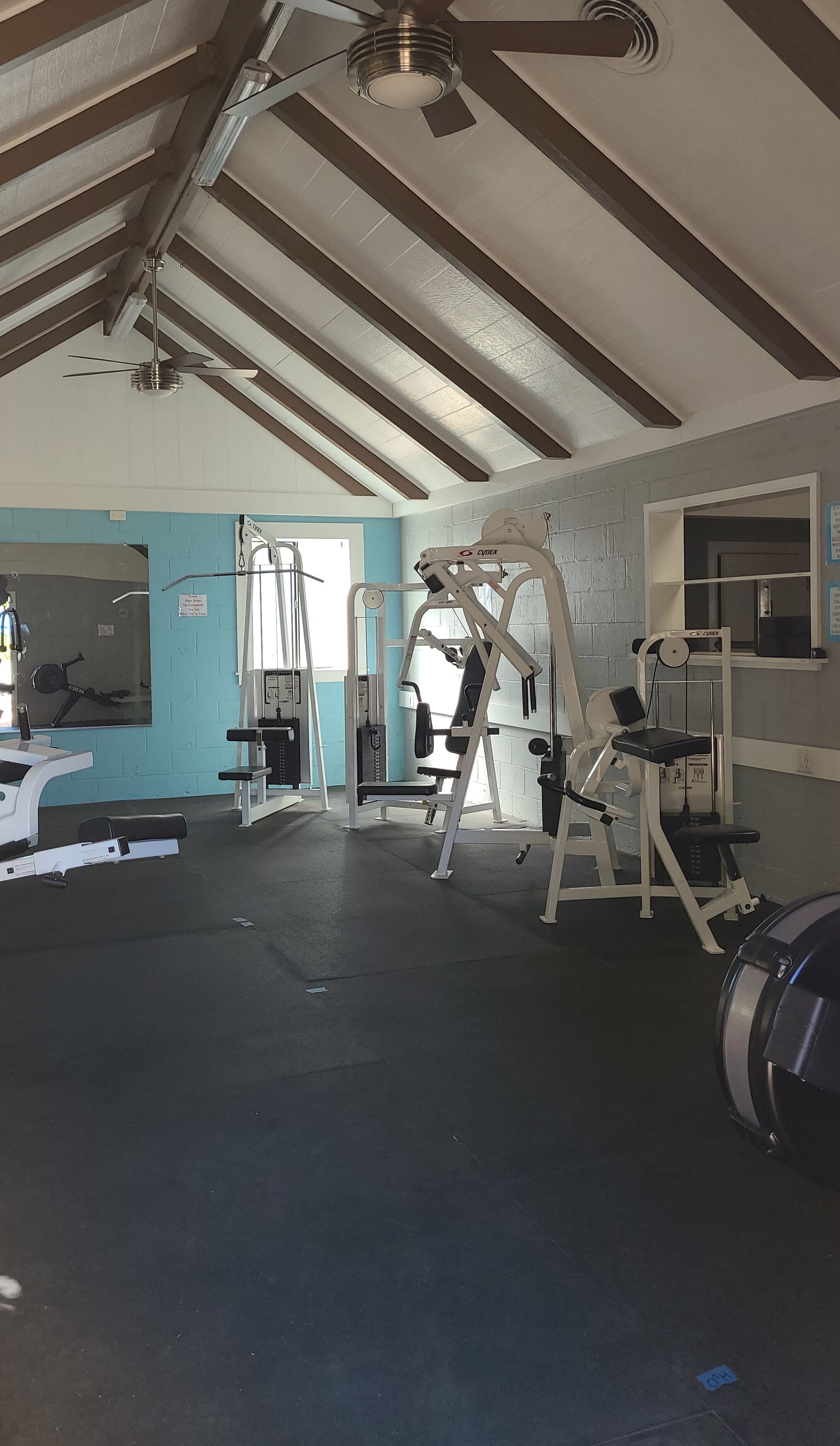 Une salle de sport dotée de ventilateurs de plafond, d’appareils d’exercice et d’un mur bleu.