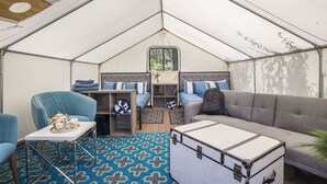 A tented accommodation with a sofa, armchairs, a small table with a tray, and a suitcase. - Surrey Resort  (Guerneville)