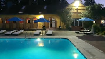 A swimming pool with lounge chairs and umbrellas, a building with arched windows, and palm trees in the background.