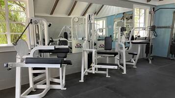 A gym with various exercise machines, large windows, and a high ceiling with exposed beams.