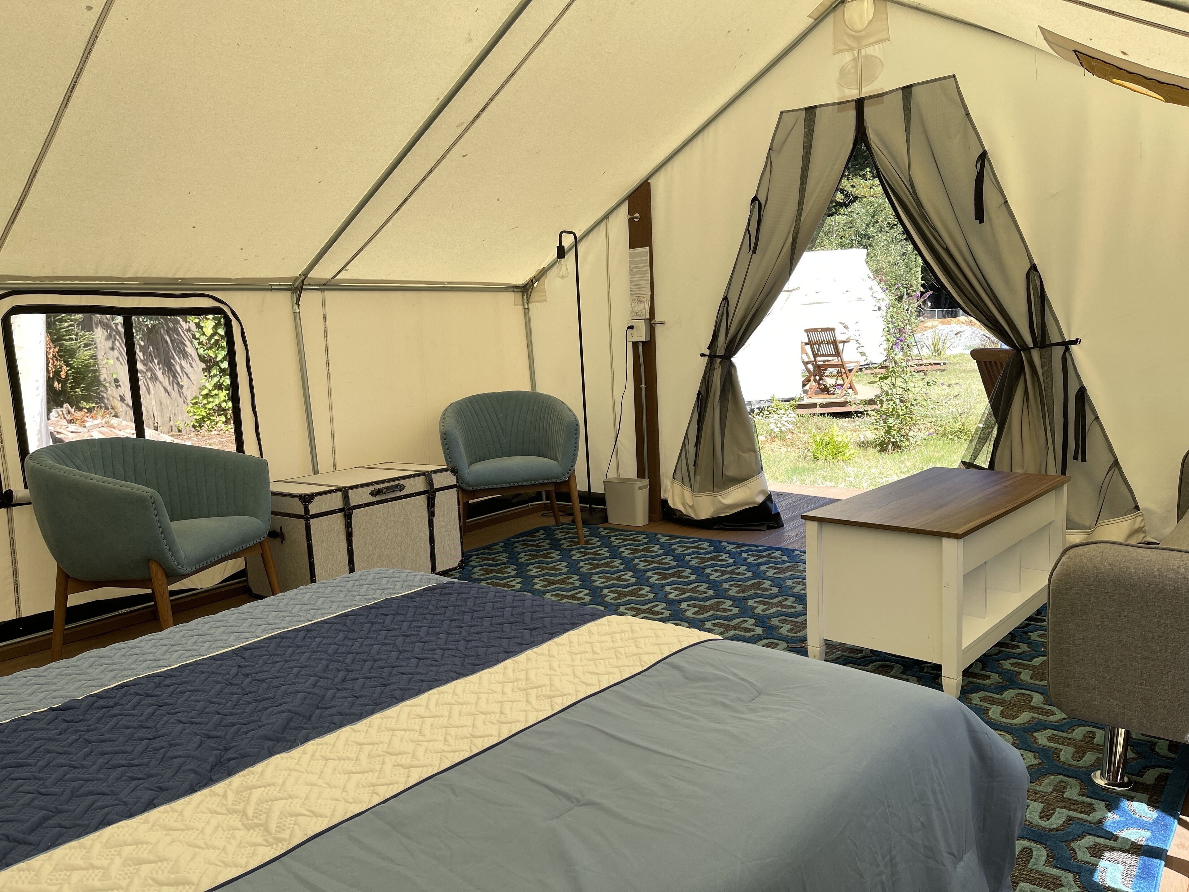 A tented room with a bed, two chairs, a small table, and a view of the outdoors.