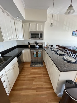 Una cocina moderna con armarios blancos, un horno de acero inoxidable, un microondas y un comedor con una mesa dispuesta para dos.