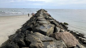 Ein felsiger Wellenbrecher, der sich ins Meer erstreckt, mit blauem Himmel.