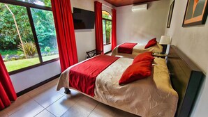 Habitación de hotel con dos camas, cortinas rojas, televisión y vista a zonas verdes.