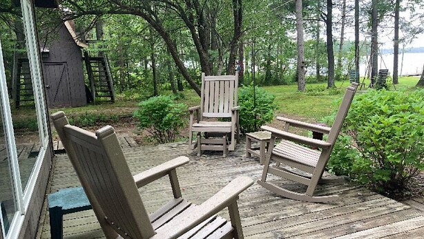 Une terrasse en bois, agrémentée de fauteuils à bascule et d’une petite table, entourée de verdure et d’une structure en bois.