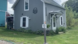 A gray cabin with a white door and window shutters, a small porch, and a sign indicating it is reserved for the cabin.