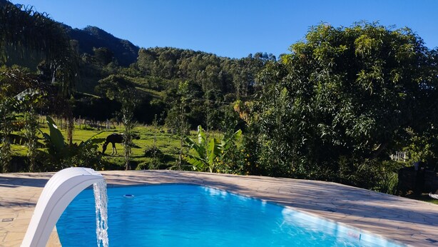 Una piscina con una cascada, rodeada de vegetación exuberante y colinas.