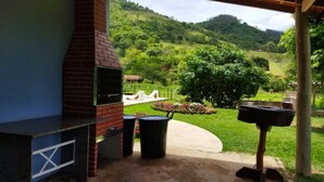 Un patio con una parrilla de ladrillo, mobiliario exterior y vistas a un paisaje verde exuberante.