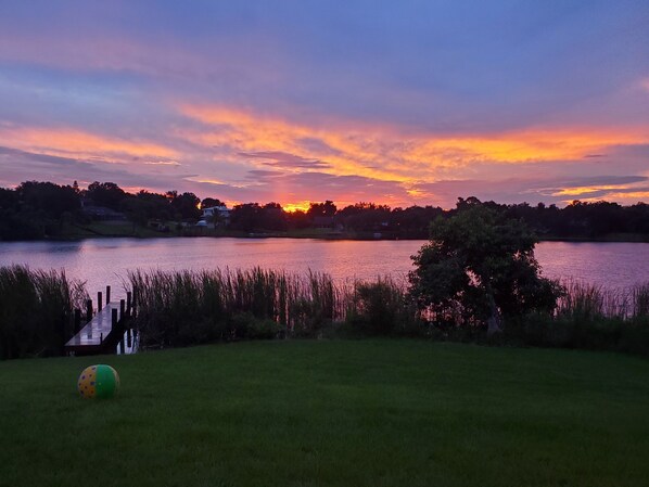 A sunset over a lake with a dock and grassy area in the foreground.