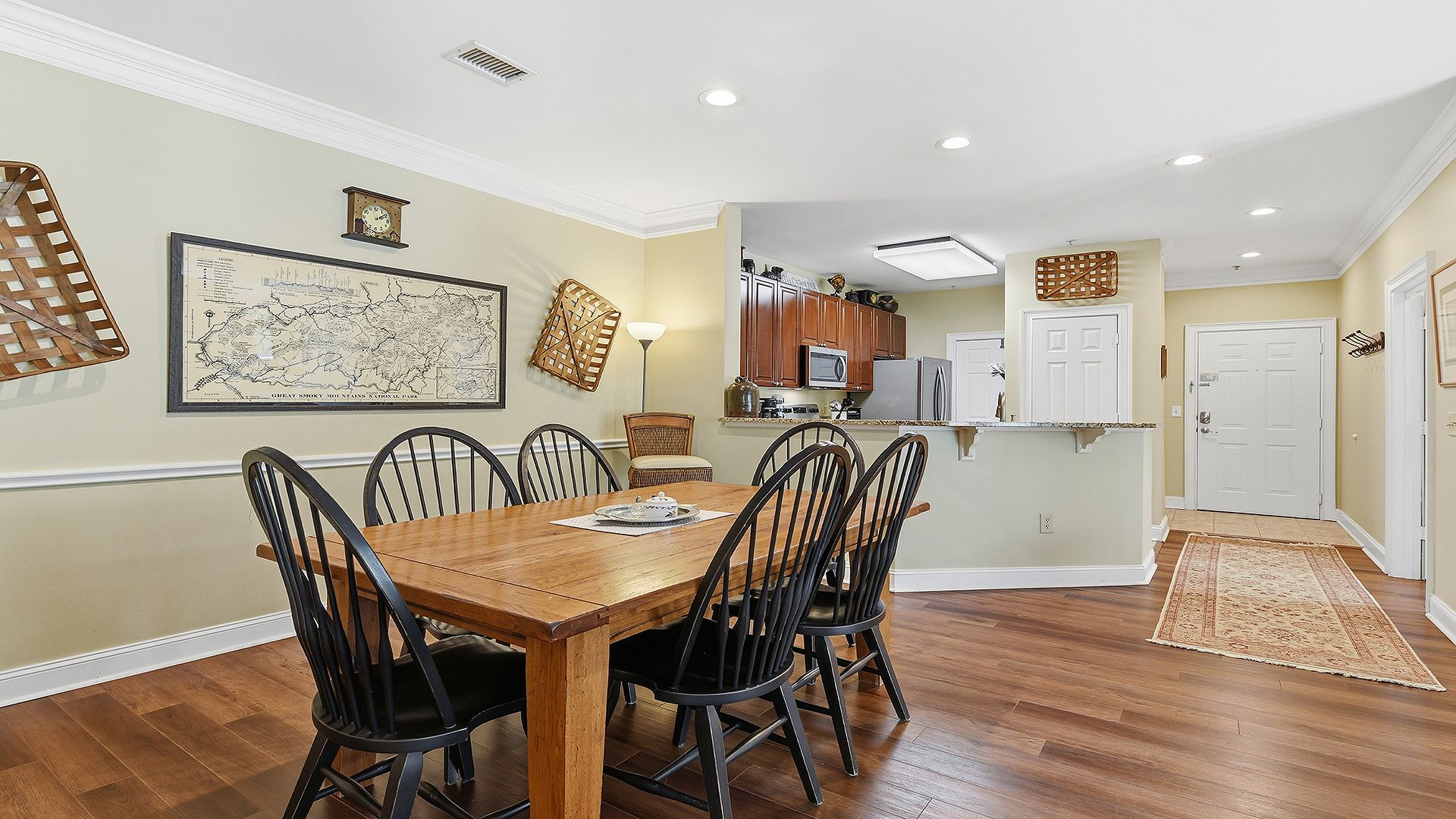 A dining area with a wooden table and chairs, a kitchen in the background, and a map on the wall.