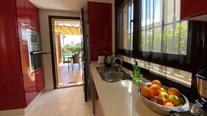 Une cuisine moderne avec des meubles de couleur rouge, un évier en acier inoxydable et un saladier rempli de fruits posé sur le plan de travail.