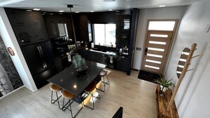 A modern kitchen with dark cabinetry, a central island, and a dining area with stools. - Modern Lux Cottage, Mtn Views, Close to Downtown (Bozeman)