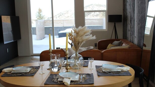 A dining area with a round table set for four, featuring a vase with pampas grass, a yellow candle, and a glass pitcher. - Modern Lux Cottage, Mtn Views, Close to Downtown (Bozeman)
