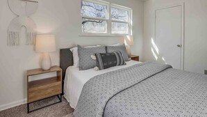 Un dormitorio con cama, mesitas de noche, ventana y puerta.