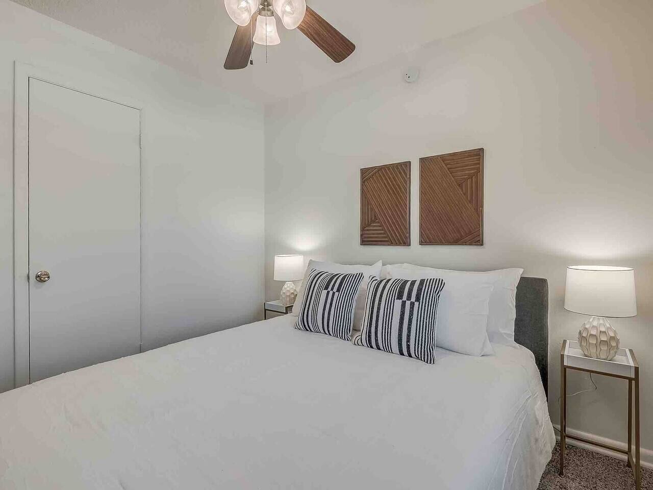 Un dormitorio con cama, dos lámparas de noche, un ventilador de techo y dos paneles en la pared.