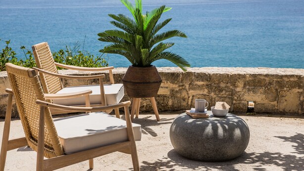 A wicker chair and a potted plant by a stone wall overlooking the sea. - Alekos Beach Houses-Eternity (Kefalonia)