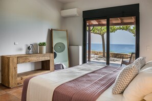 Ein Schlafzimmer mit einem Bett, einem Holztischchen, einem Spiegel und Meerblick.