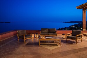 Eine Terrasse mit Gartenmöbeln, darunter zwei Sofas und ein Couchtisch, mit Blick auf ein Gewässer bei Dämmerung.