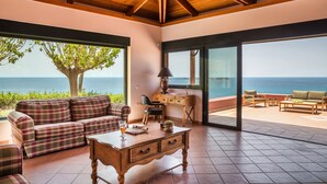 A spacious living area with a large window overlooking the sea, a wooden ceiling, and a cozy seating arrangement. - Alekos Beach Houses-Eternity (Kefalonia)