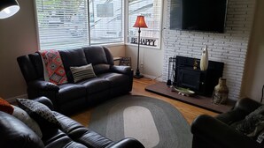 Ein Wohnzimmer mit einem schwarzen Ledersofa, einem grauen Teppich, einem Kamin und einem an einer Ziegelwand befestigten Fernseher.
