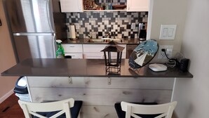 Eine Küche mit einer zentralen Kochinsel, zwei weißen Stühlen, einer Kaffeemaschine und einer Mikrowelle.
