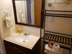 Ein Badezimmer mit Waschbecken, Spiegel, Handtuchhalter, Toilette und Regalen.