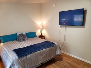 Ein Schlafzimmer mit einem Bett, einem an der Wand montierten Fernseher, einer Lampe und einem Rauchmelder.