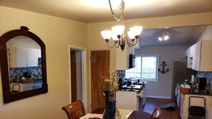 Ein Essbereich mit Holztisch und Stühlen, einer Chandelüster und Blick auf die Küche und das Wohnzimmer.