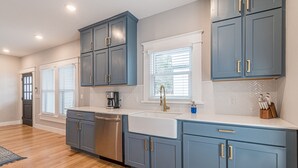 Una cocina moderna con armarios azules, lavavajillas de acero inoxidable, un lavamanos blanco y un salpicadero de azulejos tipo espiga.