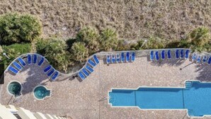 Ein Poolbereich mit Liegestühlen, die halbkreisförmig um einen zentralen Pool angeordnet sind, umgeben von einer bepflanzten Anlage mit spärlicher Vegetation.