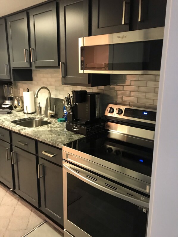 Una cocina moderna con gabinetes oscuros, estufa de acero inoxidable, microondas y horno empotrado.
