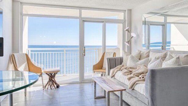 Ein modernes Wohnzimmer mit einem großen Schiebeglasfenster, das auf einen Balkon mit Meerblick führt.
