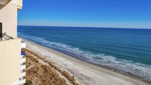 Blick auf einen Strand mit blauem Himmel, sandigem Ufer und einem Gebäude direkt am Strand.