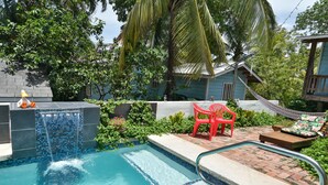 A swimming pool with a small waterfall feature, surrounded by lush greenery and a hammock. - In the heart of West End, Roatan - Mariposa Lodge - Unit 2 (West End)