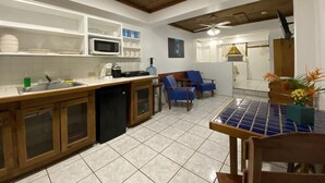 A kitchen with a wooden ceiling, white cabinets, a microwave, and a sink. There is a dining area with blue chairs and a table. - In the heart of West End, Roatan - Mariposa Lodge - Unit 2 (West End)