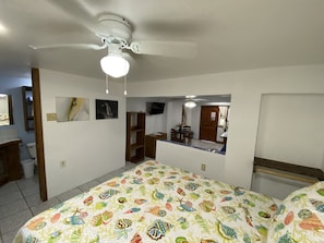 A bedroom with a bed, a ceiling fan, a TV, and a small dining area.