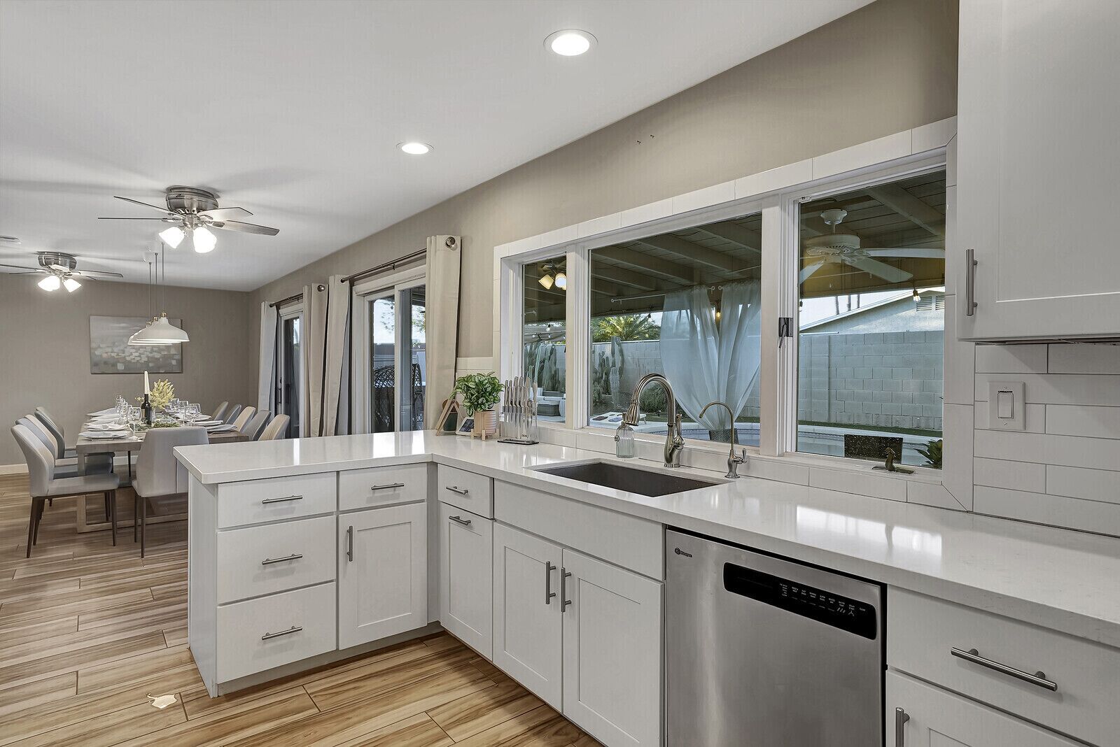 A modern kitchen with white cabinetry, a stainless steel dishwasher, and a large window offering a view of the outdoors.