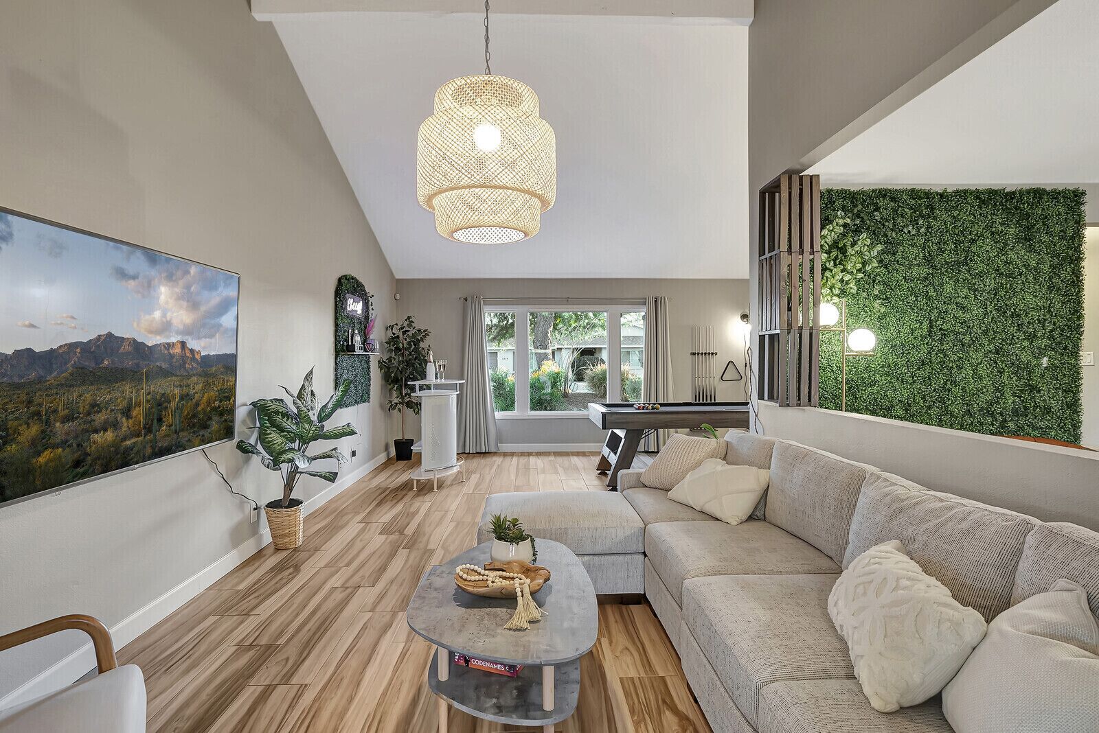 A modern living room with a large painting, a hanging light fixture, a green wall, and a pool table.