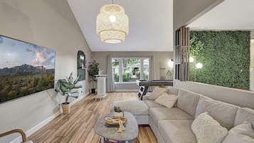 A modern living room with a large painting, a hanging light fixture, a green wall, and a pool table.