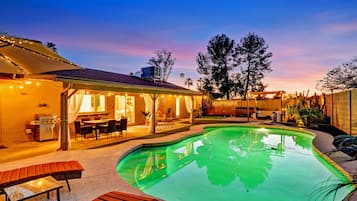 A backyard with a swimming pool, outdoor furniture, and a covered patio area.