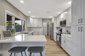 A modern kitchen with white cabinets, a central island with bar stools, stainless steel appliances, and a view of the outdoors. - Scottsdale Gem - Pickleball/Pool/Jacuzzi/Golf 10mins to Kierland Commons (Scottsdale)