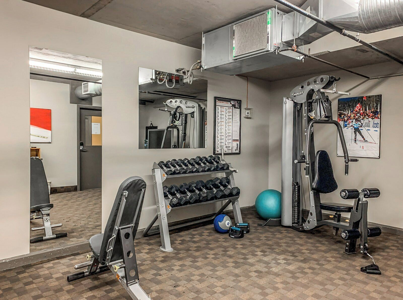 Ett gym med träningsutrustning, en spegel som hänger på väggen och en dörr som leder till ett annat rum.