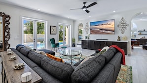Ein geräumiges Wohnzimmer mit einem großen, grauen Sofa, einem Glastisch und einem flachbildfernseher an der Wand.