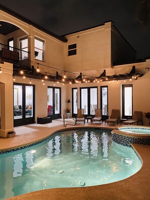 Un espace piscine doté d’un jacuzzi, de coins salon extérieurs et de guirlandes lumineuses.
