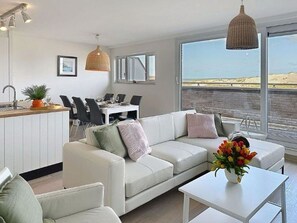 Un salon moderne avec un canapé blanc, une table à manger et des chaises. On y trouve également un coin cuisine équipé d’un évier et d’un luminaire suspendu.