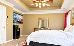 A hotel room with a bed, a television mounted on the wall, a ceiling fan, and a minibar.