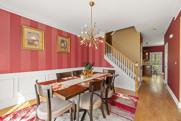 Un espace repas comprenant une table et des chaises en bois, un lustre et un escalier.