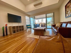Relax in this stylish living room with a large flat-screen TV, comfortable sofa, and glass door leading to a balcony.