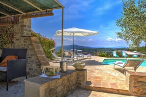 A stone patio with outdoor seating, a pool, and a view of distant mountains.