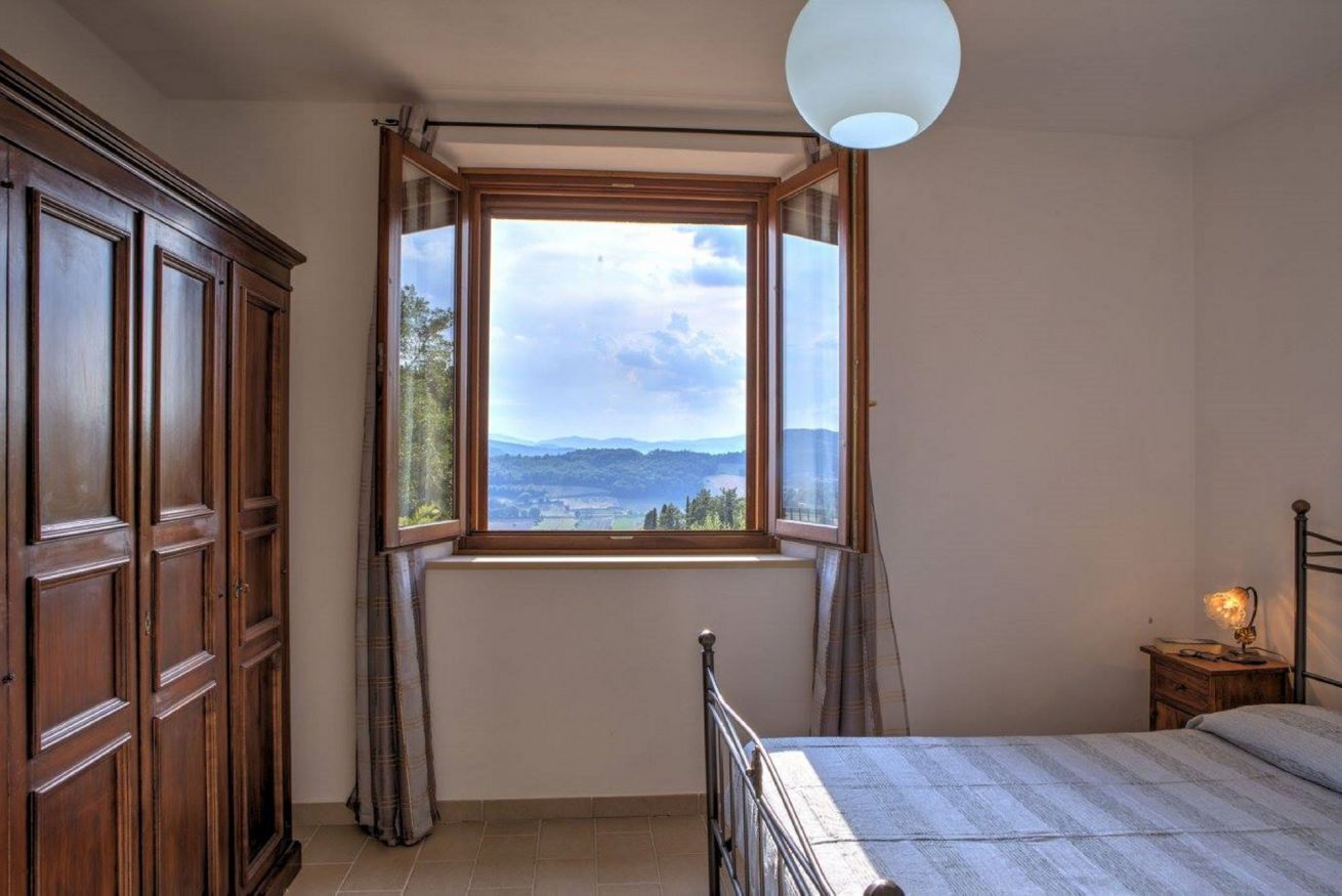 Une chambre avec une grande fenêtre, un lit, une table de chevet et une armoire.